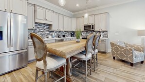 A modern kitchen with white cabinets, stainless steel appliances, a wooden dining table, and patterned chairs. - Beautiful White Coral Chateau (Miramar Beach)
