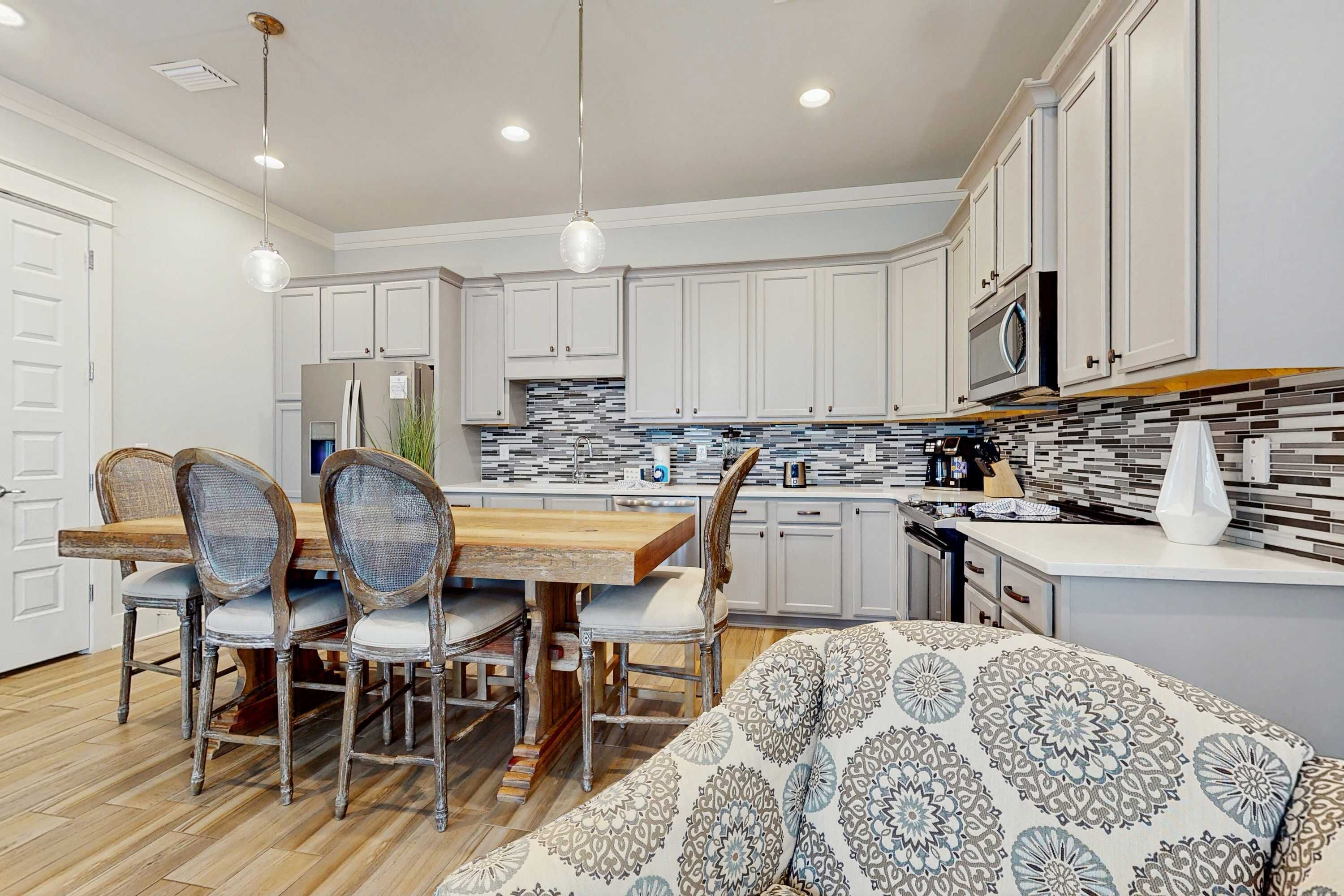 A modern kitchen with white cabinets, a wooden dining table, and a patterned sofa.