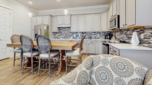 A modern kitchen with white cabinets, a wooden dining table, and a patterned sofa. - Beautiful White Coral Chateau (Miramar Beach)