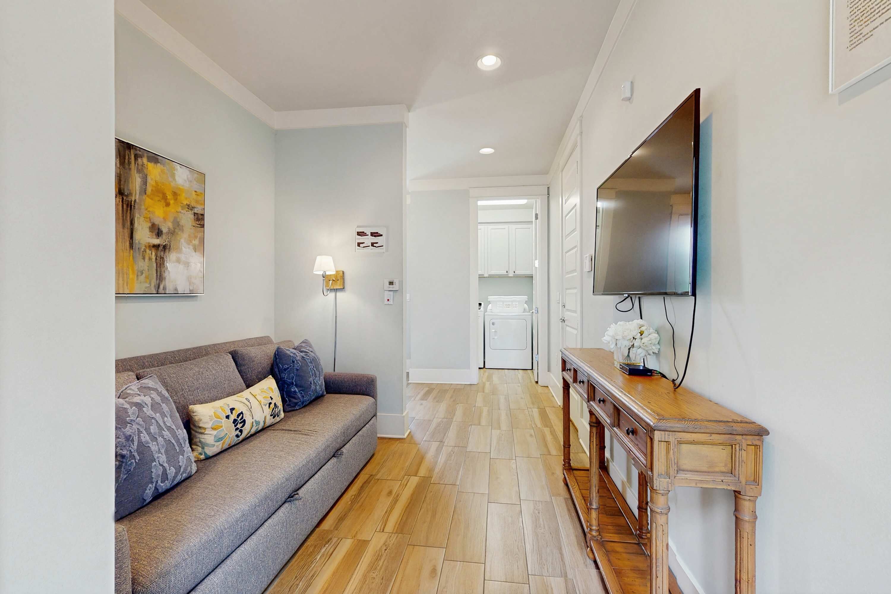 A modern living room with a grey sofa, wooden console table, and a flat-screen TV mounted on the wall.