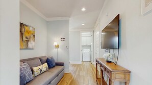 A modern living room with a grey sofa, wooden console table, and a flat-screen TV mounted on the wall. - Beautiful White Coral Chateau (Miramar Beach)