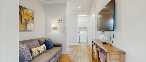 A modern living room with a grey sofa, wooden console table, and a flat-screen TV mounted on the wall.