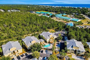 An aerial view of a residential area with multiple houses, a swimming pool, and a large body of water in the background. - Charming townhouse with Wifi, Shared pool, Washer and Dryer (Santa Rosa Beach)
