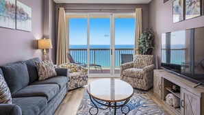 Un salon comprenant un canapé, deux fauteuils, une table basse, un téléviseur et un balcon avec vue sur l’océan.