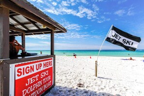 Une plage avec un panneau indiquant la présence de jet-skis et un autre panneau proposant des excursions d’observation des dauphins.