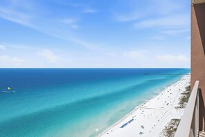 A beach view from a balcony with clear skies, a pier in the distance, and a sandy shoreline.