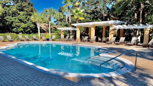 A swimming pool with lounge chairs and a pergola, surrounded by trees.