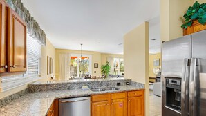 A modern kitchen with granite countertops, wooden cabinets, a stainless steel refrigerator, and a built-in dishwasher.