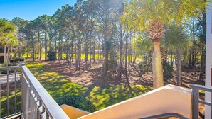 A view from a balcony overlooking a landscaped area with trees and a palm tree, with a clear blue sky.
