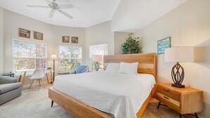 A bedroom with a wooden bed, a desk, a chair, a nightstand with a lamp, and a ceiling fan.