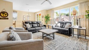 A living room with two black leather sofas, a grey armchair, a coffee table, and a ceiling fan.