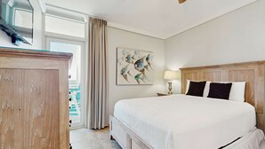 Habitación de hotel con una cama grande, cabecera de madera, un cuadro en la pared, una lámpara y vistas al exterior.
