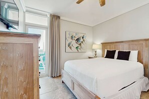 A hotel room with a large bed, a wooden headboard, a painting on the wall, a lamp, and a view of the outside. - Spacious Rental W/ Views Of The Gulf, Beach Service, Walk To Restaurants (Fort Walton Beach)