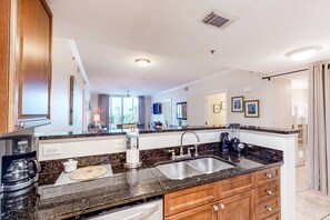 A modern kitchen with granite countertops, a double sink, and wooden cabinetry. - Welcoming Condo On Okaloosa Island Children's Playground, 2 Hot Tubs (Fort Walton Beach)