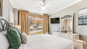 A hotel room with a large bed, a ceiling fan, a TV, a dresser, and a balcony with curtains. - Ground-Floor Condo At Waterscape 490 Feet Of Private Beach (Fort Walton Beach)