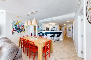 A modern kitchen with a central island, pendant lighting, and a dining area with red chairs. - Beachfront Condo with Private Beach/Access, Balcony, Ocean View, & WiFi (Fort Walton Beach)