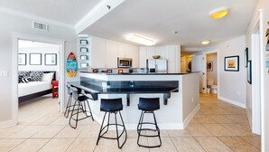 A modern kitchen with a central island, bar stools, and a microwave. - Beachfront Condo with Private Beach & Access, Balcony, Ocean View, & WiFi (Fort Walton Beach)
