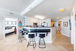A modern kitchen with a central island, bar stools, and a microwave. - Beachfront Condo with Private Beach/Access, Balcony, Ocean View, & WiFi (Fort Walton Beach)