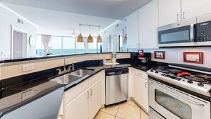 A modern kitchen with a dishwasher, stove, microwave, and a large sink. - Beachfront Condo with Private Beach & Access, Balcony, Ocean View, & WiFi (Fort Walton Beach)