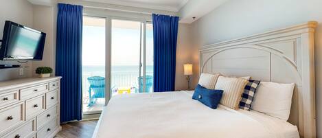 A hotel room with a large bed, a television, a dresser, and a balcony with blue curtains.