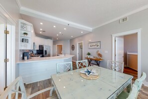 A spacious kitchen with white cabinetry, a central island, and a dining area with a marble table and white chairs. - Incredible Gulf-Front Condo On Okaloosa Island 490 Feet Of Private Beach (Fort Walton Beach)