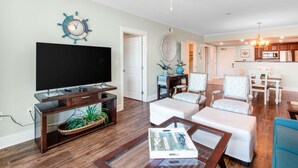 A living room with a flat-screen TV, wooden entertainment center, and a ceiling fan. - Beach-Chic Condo On Okaloosa Island Steps To Beach Lazy River (Fort Walton Beach)
