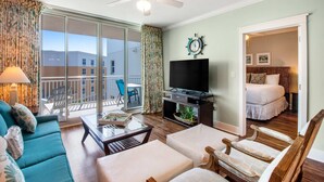 A hotel room with a balcony, a TV, a bed, and a seating area with a table and chairs. - Beach-Chic Condo On Okaloosa Island Steps To Beach Lazy River (Fort Walton Beach)