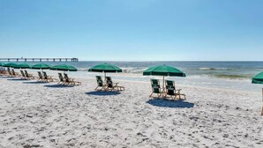 A beach with rows of green umbrellas and wooden lounge chairs. - Beach-Chic Condo On Okaloosa Island Steps To Beach Lazy River (Fort Walton Beach)