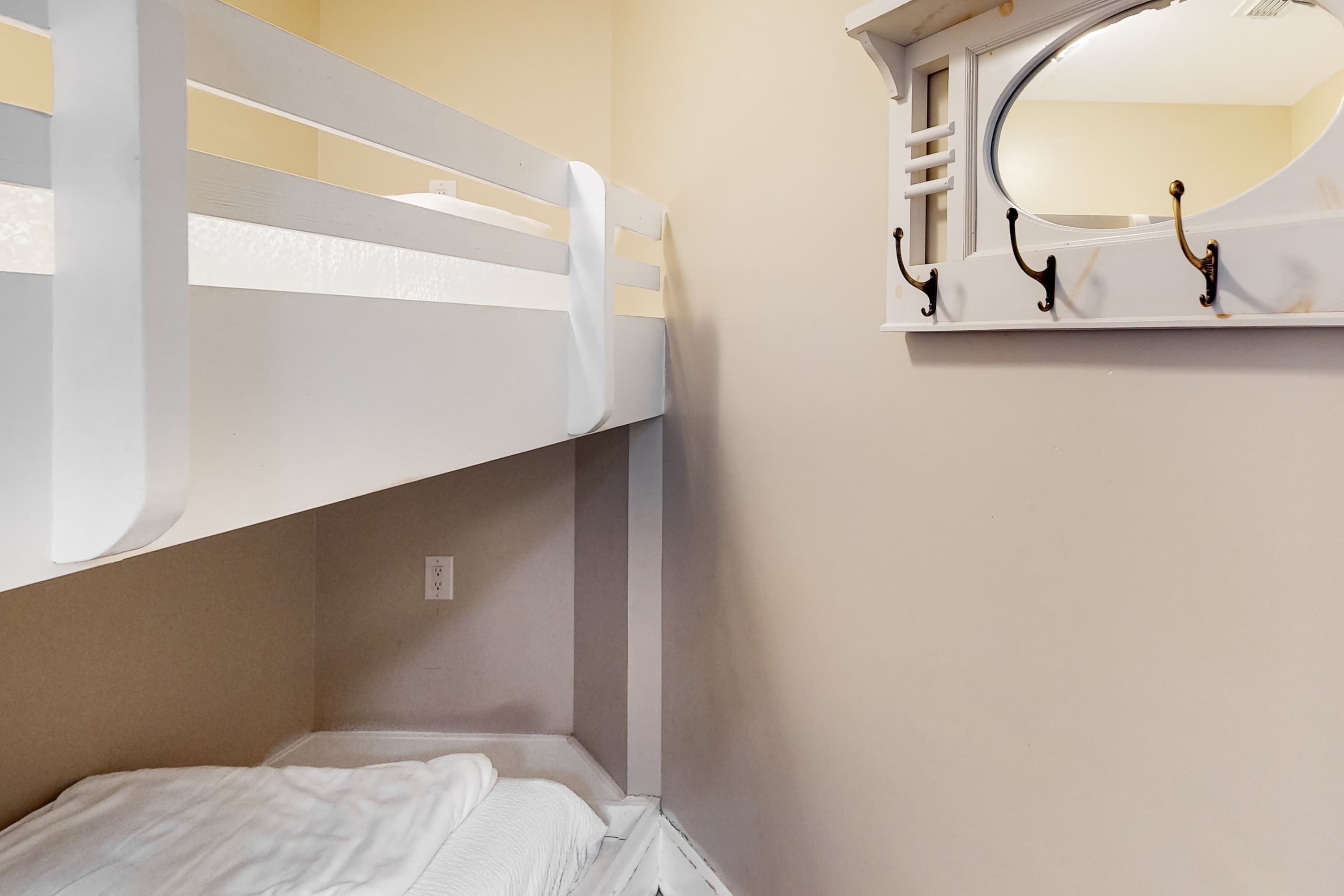 A bunk bed with a white headboard, a small bedside table, and a mirror with three hooks.