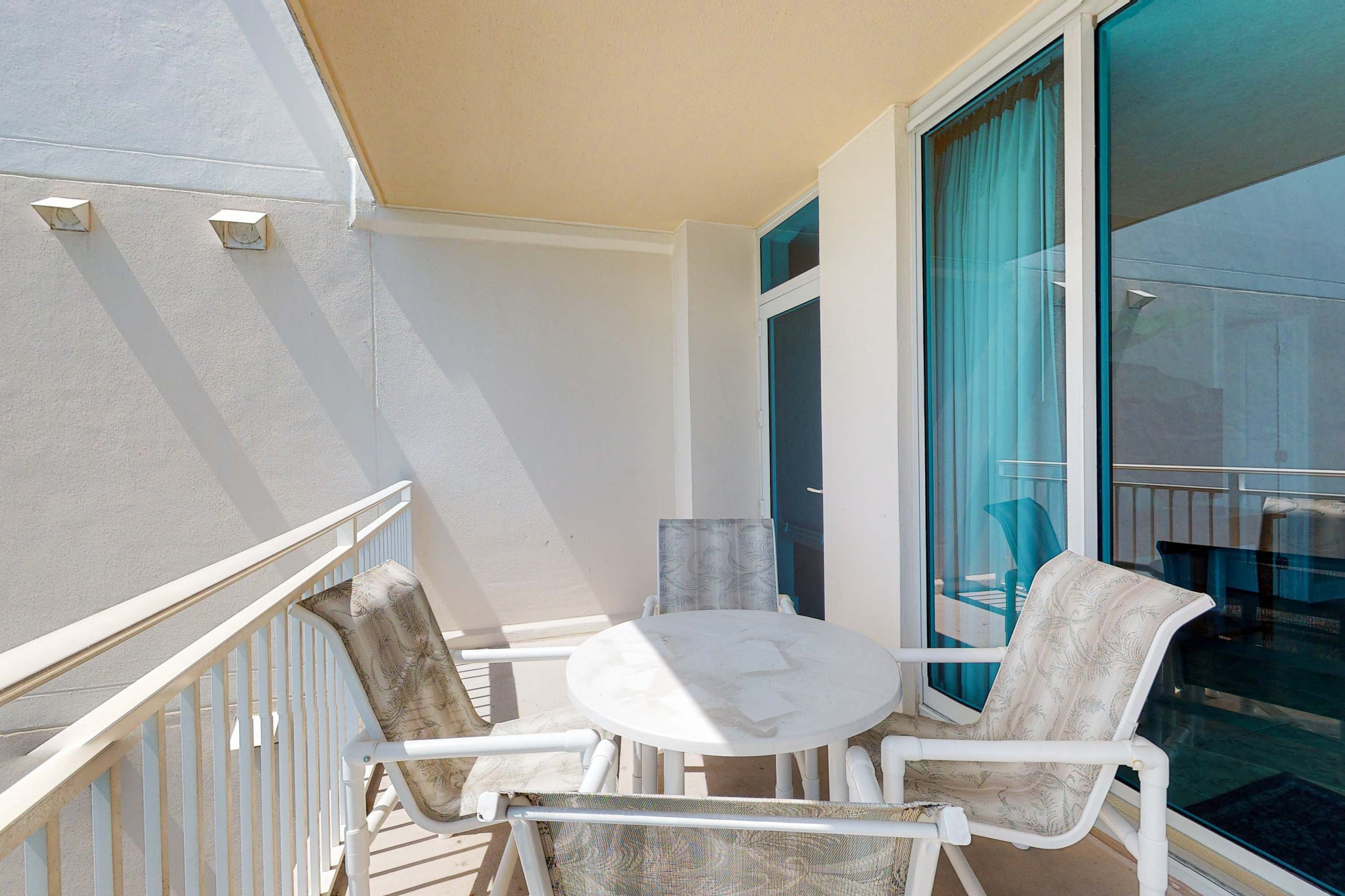 A balcony with a white table and chairs, a glass door, and a view of the outside.