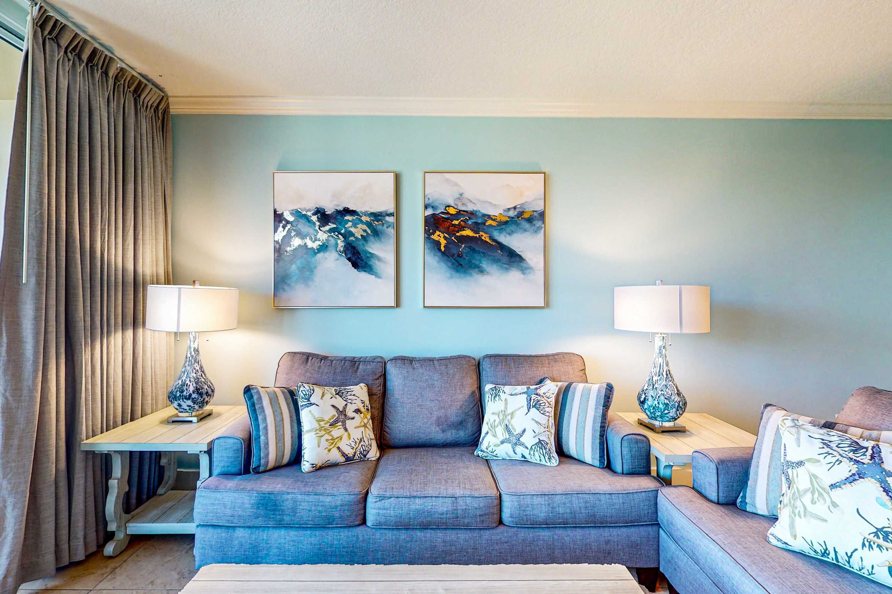 A living room with a grey sofa, two side tables with lamps, and two abstract paintings on the wall.
