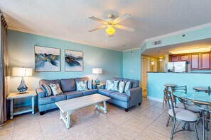 A living room with a sectional sofa, a coffee table, and a dining area with a glass table and chairs. - Snowbird-friendly condo on Okaloosa Island with lazy river - steps to beach (Fort Walton Beach)