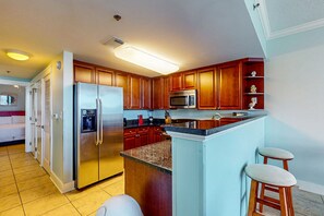 A kitchen with wooden cabinets, stainless steel appliances, a granite countertop, and a built-in island with stools. - Snowbird-friendly condo on Okaloosa Island with lazy river - steps to beach (Fort Walton Beach)
