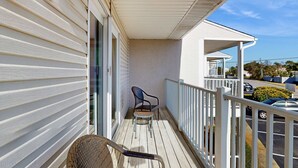 En balkon med hvide gelændere, en fletstol og et lille bord.