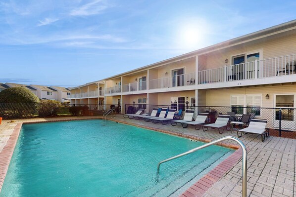 A hotel with a swimming pool, lounge chairs, and a fenced deck area. - Comfy townhome with pool, patio, WiFi, & W/D - walkable location to the beach (Miramar Beach)