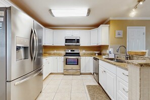 A modern kitchen with stainless steel appliances, white cabinets, and a granite countertop. - Comfy townhome with pool, patio, WiFi, & W/D - walkable location to the beach (Miramar Beach)