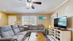 En stue med en modulsofa, et sofabord, et fjernsyn på et skab og en loftventilator.