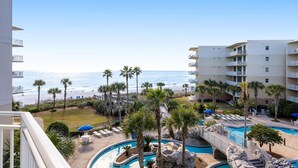 Un área de piscina en un resort, con vistas a la playa, palmeras y un edificio de varios pisos.