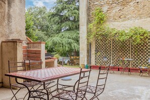 Eine Terrasse mit einem Metalltisch, Stühlen, einem Backofen aus Ziegeln und einer Steinmauer.