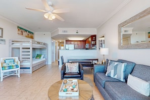 A living room with a sofa, a coffee table with decorative items, a bunk bed, and a kitchen area in the background. - 6th Floor Condo On Okaloosa Island Waterfall, Lazy River (Fort Walton Beach)