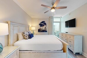 A bedroom with a bed, a ceiling fan, a TV, and a window with a view of buildings. - 4th-floor remodeled condo with pool, hot tub, fitness room, balcony & lazy river (Fort Walton Beach)