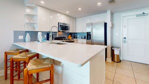 Cozinha moderna com armários brancos, uma ilha grande com banquetas, eletrodomésticos de aço inoxidável e backsplash de azulejo.