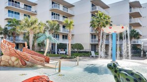 Zona de piscina de hotel con tobogán de agua, estatua de rana y área de juegos cubierto con red.