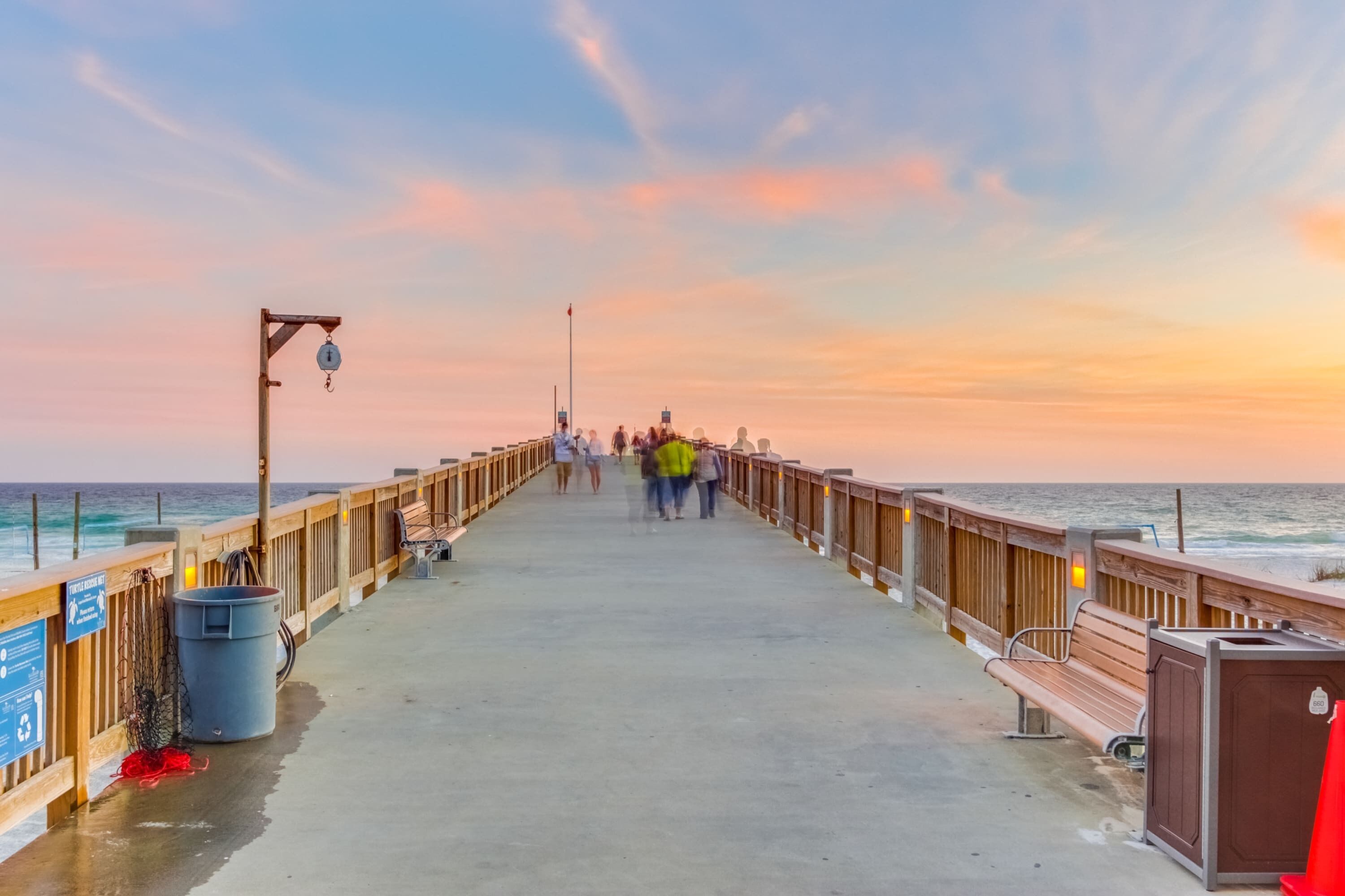 A pier with a wooden railing, benches, and a trash bin.