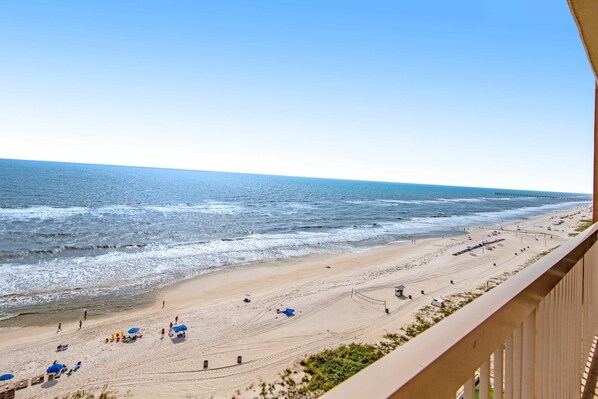 A beach with umbrellas, people, and a pier in the distance. - 12th-floor, waterfront condo with pools, grills & fitness center (Panama City Beach)