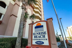 A sign for Sunrise Beach Condominium with a building in the background. - 12th-floor, waterfront condo with pools, grills & fitness center (Panama City Beach)