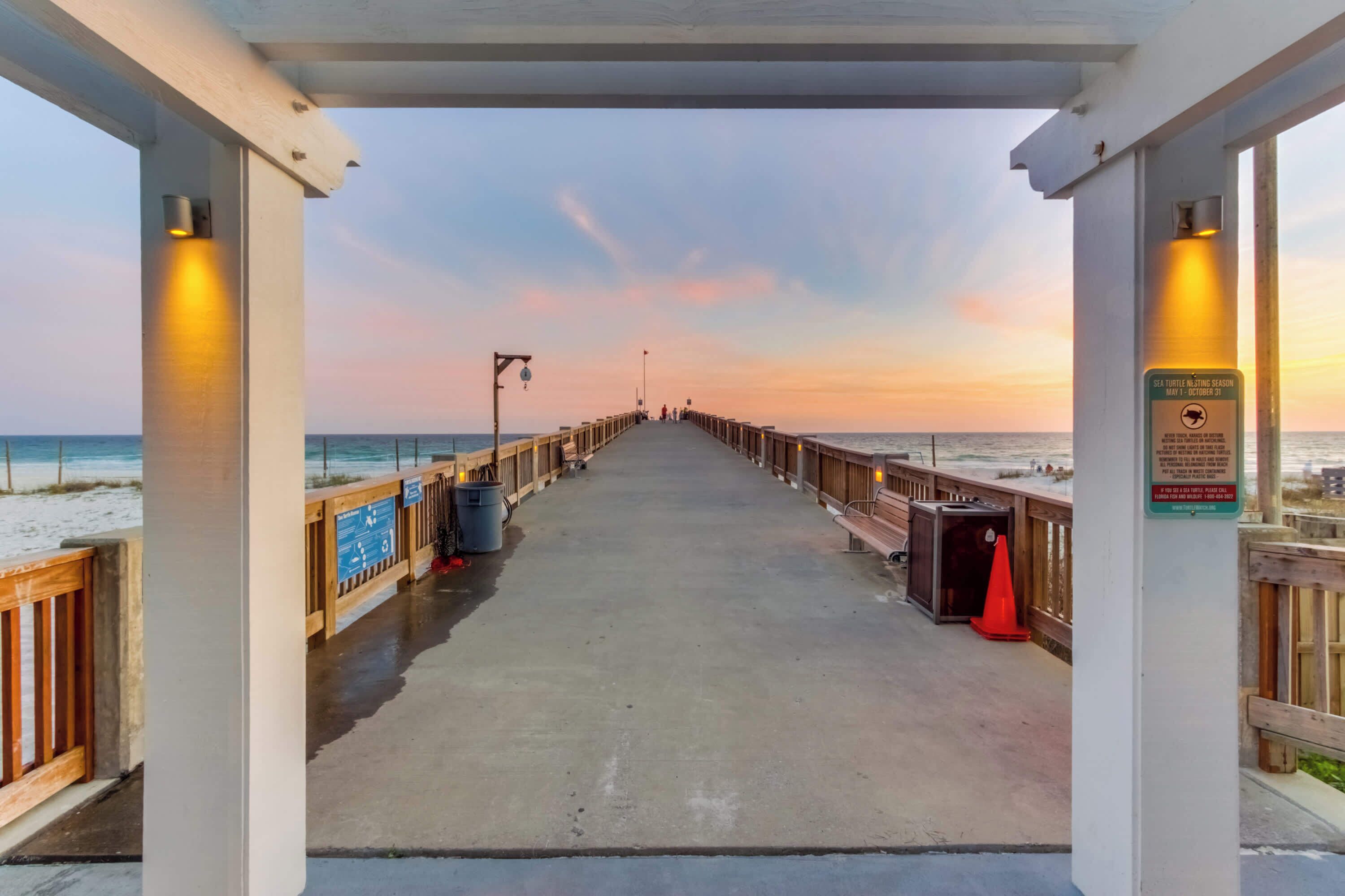 A pier with a concrete walkway, wooden railings, and a sign indicating a turtle nesting season.