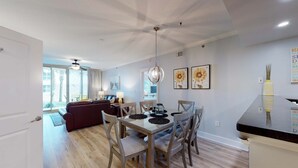 A modern dining area with a glass table, wooden chairs, and a ceiling fan. - Handicap accessible ground-floor condo on Okaloosa Island Waterfall, Lazy River (Fort Walton Beach)