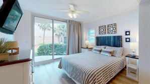 A bedroom with a bed, a ceiling fan, a TV, a window with curtains, and artwork on the wall. - Handicap accessible ground-floor condo on Okaloosa Island Waterfall, Lazy River (Fort Walton Beach)