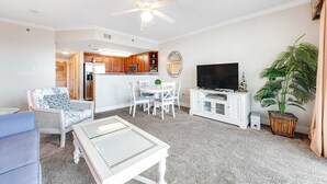 A living room with a ceiling fan, a TV, a dining table with chairs, a sofa, and a kitchen in the background. - 6th Floor Cozy, 'At Home' Condo At Waterscape Steps To Beach Lazy River (Fort Walton Beach)
